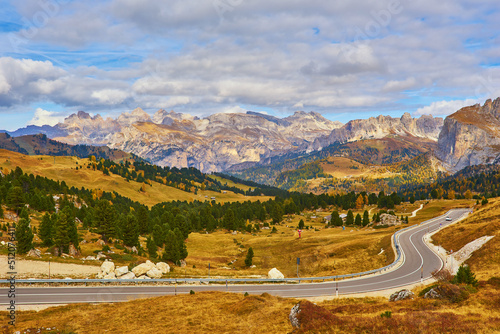 Autumn scene with curved road and yellow larches from both sides in alp forest. Dolomite Alps. Italy