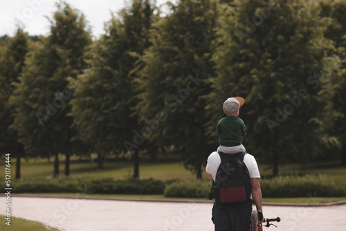 A man and a boy go for a walk with a backpack for hiking. Portrait of a father and son sitting on their father's shoulders in the park. The concept of travel and family. photo