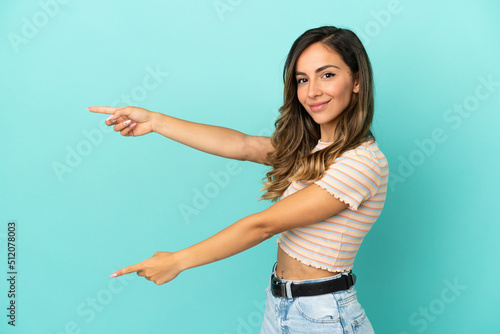 Young woman over isolated blue background pointing finger to the side and presenting a product