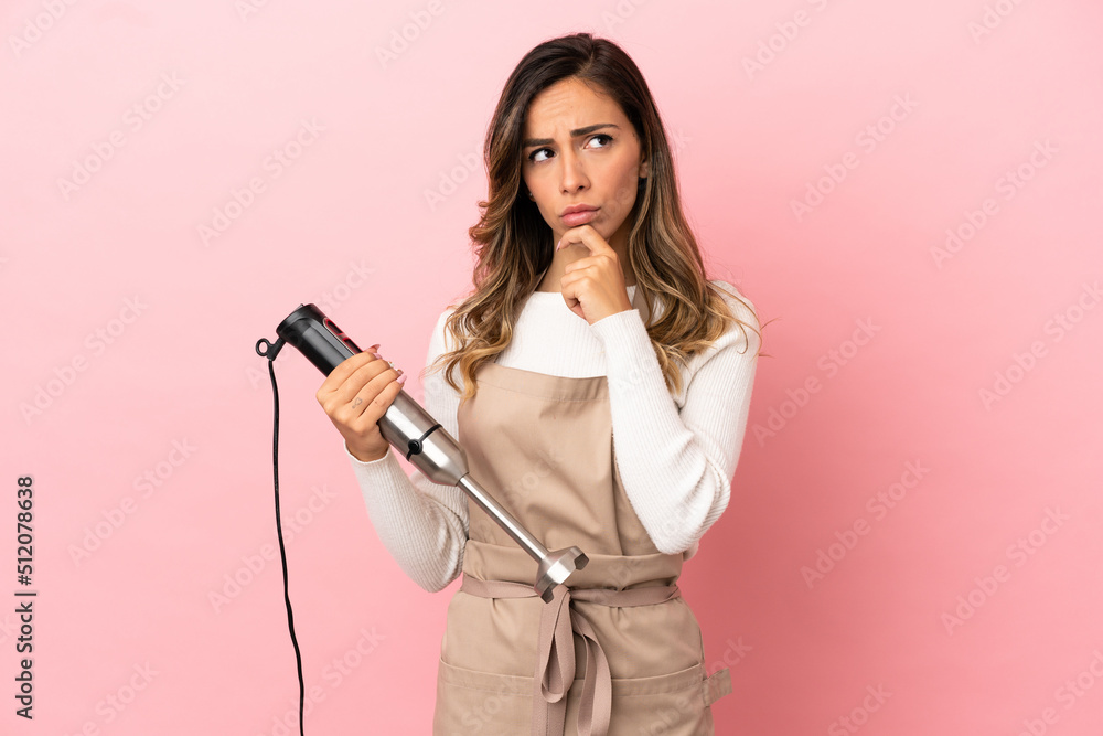 Young woman using hand blender over isolated pink background having doubts and thinking Young woman using hand blender over isolated pink background having doubts and thinking