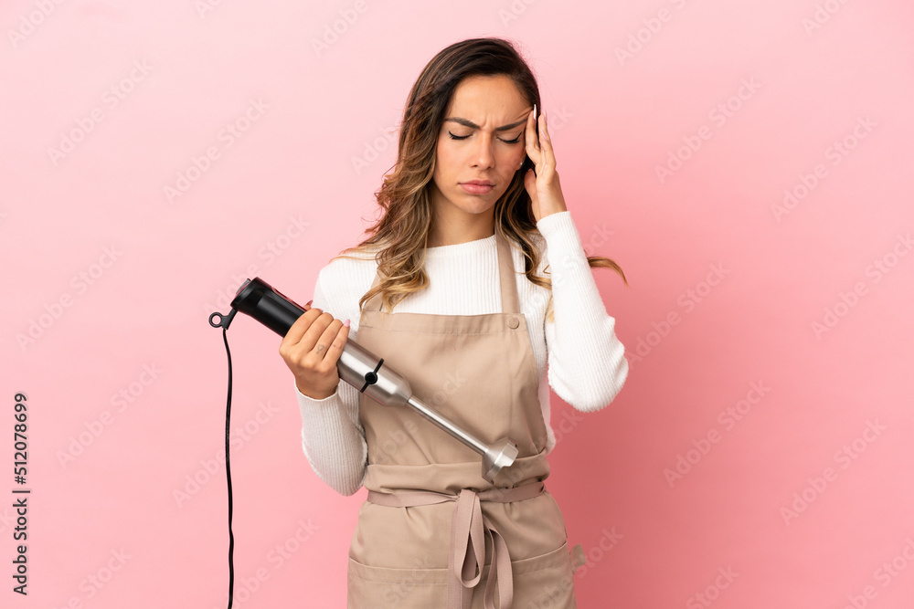 Young woman using hand blender over isolated pink background with headache Young woman using hand blender over isolated pink background with headache