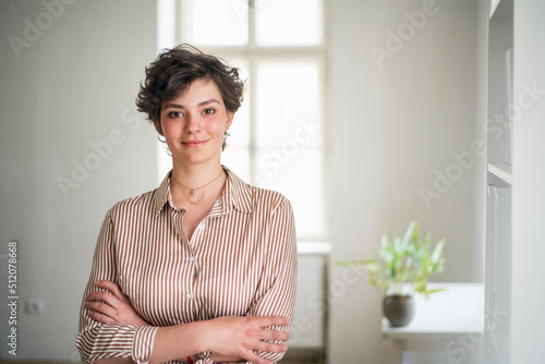Free Download Happy young woman student standing in front of window in office. Looking in camera. - GFXLoad