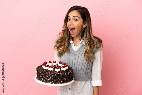 Young woman holding birthday cake over isolated pink background with surprise facial expression
