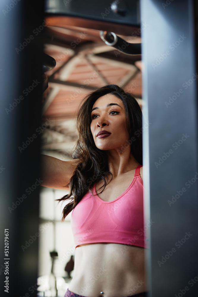 A strong female bodybuilder is doing pull-ups on a machine in a gym. A strong female bodybuilder is doing pull-ups on a machine in a gym.