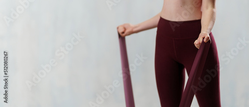 Close-up of sports woman in fashion sportswear exercising with elastic band stretch over greay background. photo