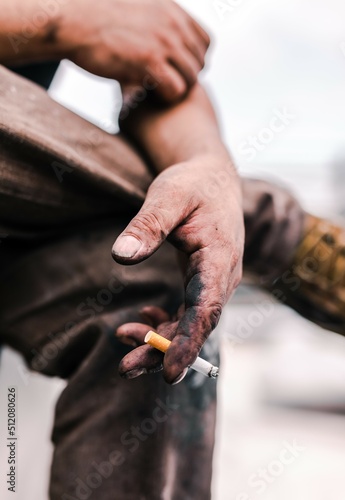 A dirty hand holding a smoking cigarette