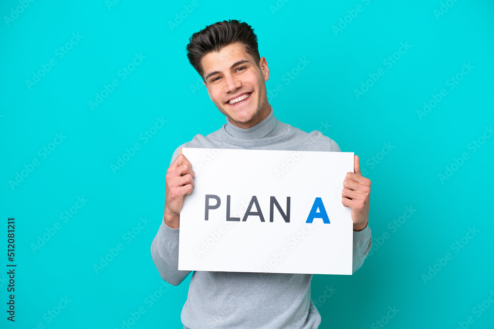 Young handsome caucasian man isolated on blue bakcground holding a placard with the message PLAN A Young handsome caucasian man isolated on blue bakcground holding a placard with the message PLAN A