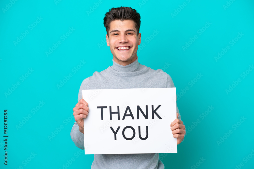 Young handsome caucasian man isolated on blue bakcground holding a placard with text THANK YOU with happy expression Young handsome caucasian man isolated on blue bakcground holding a placard with text THANK YOU with happy expression