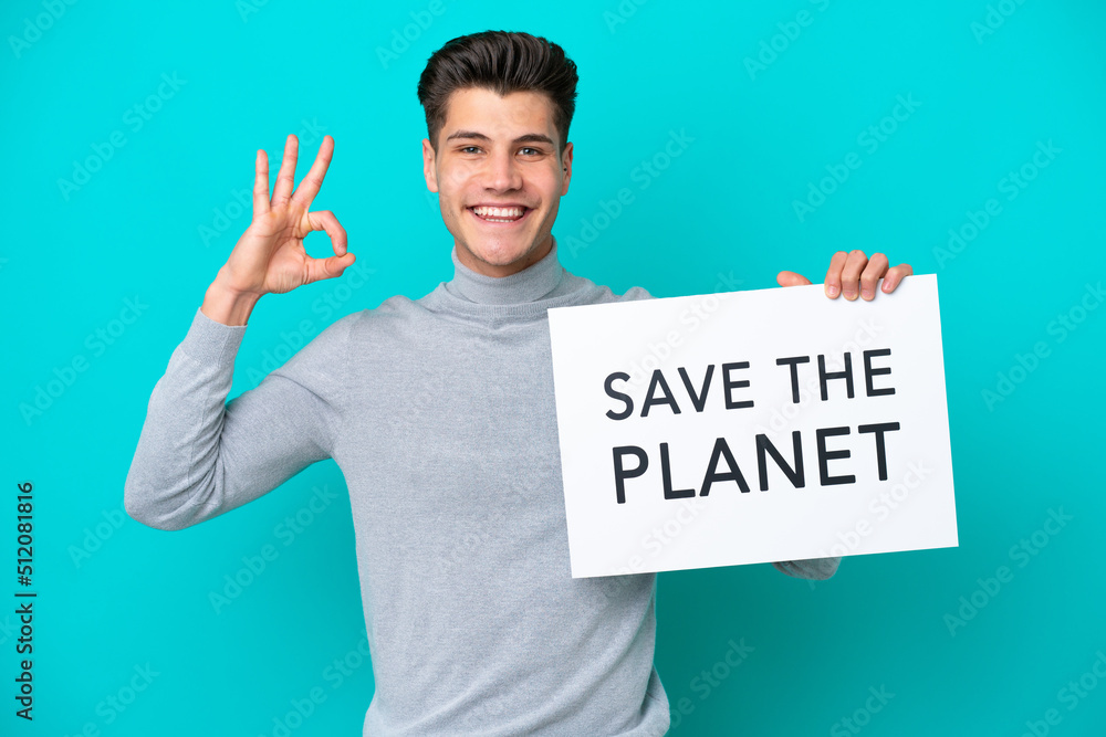Young handsome caucasian man isolated on blue bakcground holding a placard with text Save the Planet and celebrating a victory Young handsome caucasian man isolated on blue bakcground holding a placard with text Save the Planet and celebrating a victory