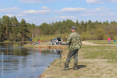 A man is fishing on the river. Fisherman on the shore, camouflage clothing. Beach, river bank