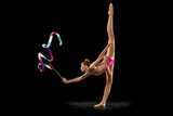 One young sportive girl, rhythmic gymnastics artist performing with ribbon isolated on dark background. Concept of sport, action, aspiration, education, active lifestyle