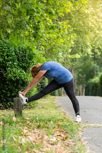Vertical view of unrecognizable adult woman stretching legs sorrounded by nature in a park