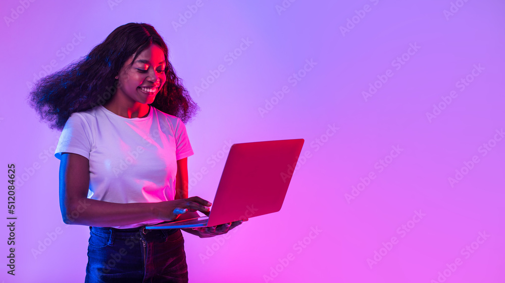 Portrait of young black woman using laptop pc, studying or working remotely, having online conference in neon light Portrait of young black woman using laptop pc, studying or working remotely, having online conference in neon light