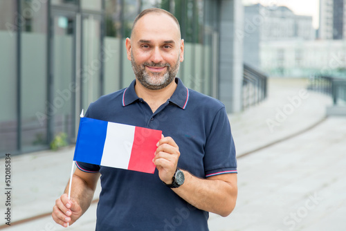 Middle-aged man with a French flag in front of city buildings.