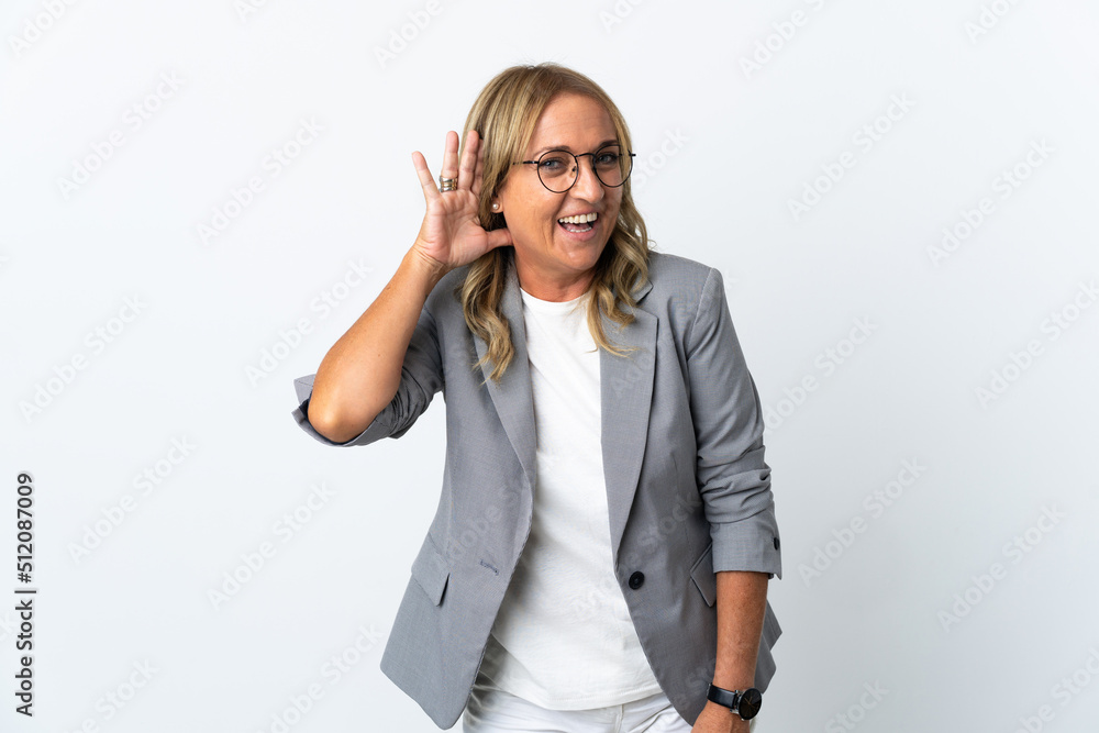 Middle aged business woman over isolated white background listening to something by putting hand on the ear