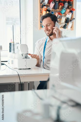Cheerful male fashion designer speaking on cell phone at work