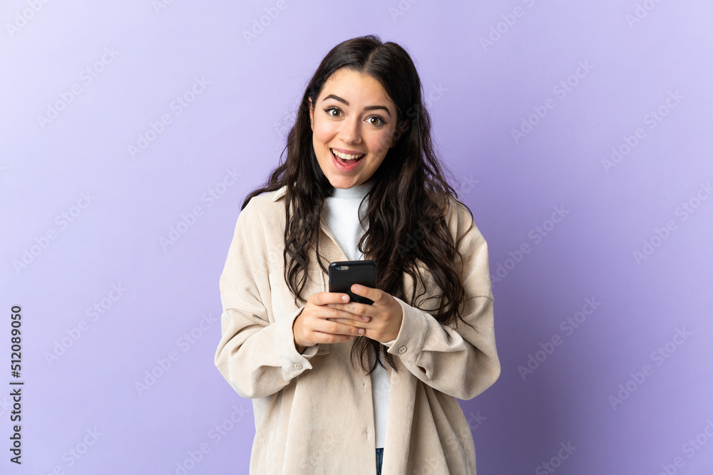 Young caucasian woman isolated on purple background surprised and sending a message Young caucasian woman isolated on purple background surprised and sending a message