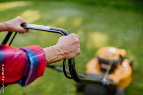 Close-up of elderly woman mowing grass with lawn mower in the garden, garden work concept.