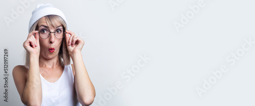 Surprised young woman in a white hat holds glasses on a light background. Banner