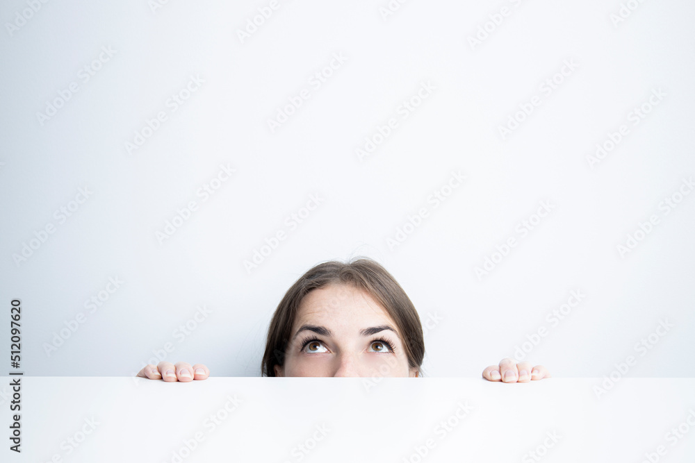 Young woman looking up from under a white table against a white wall Young woman looking up from under a white table against a white wall