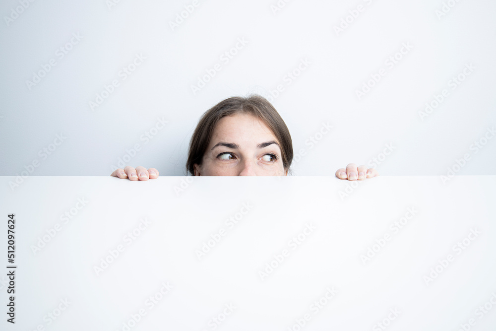 Young woman looking to the side looking out from under a white table against a white wall Young woman looking to the side looking out from under a white table against a white wall