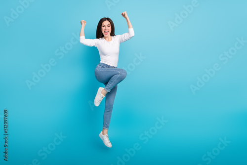Photo of funny lucky woman wear white shirt rising fists jumping high empty space isolated blue color background © deagreez
