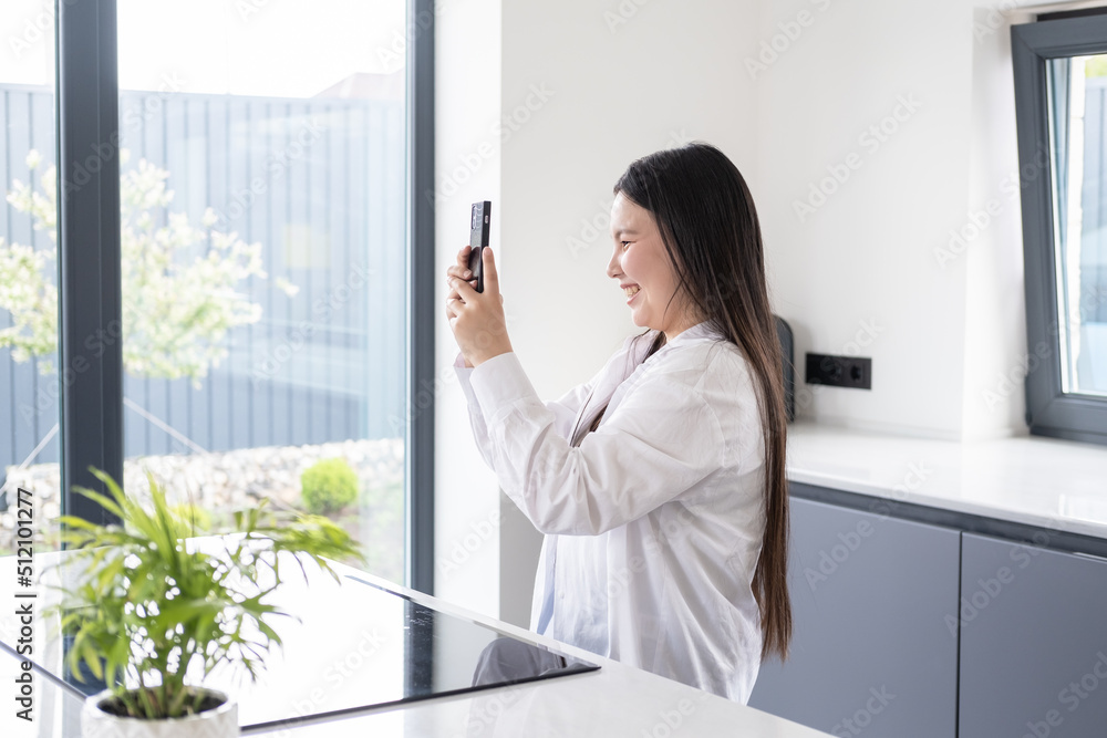 beautiful smiling young asian woman with dark long hair using phone at modern interior