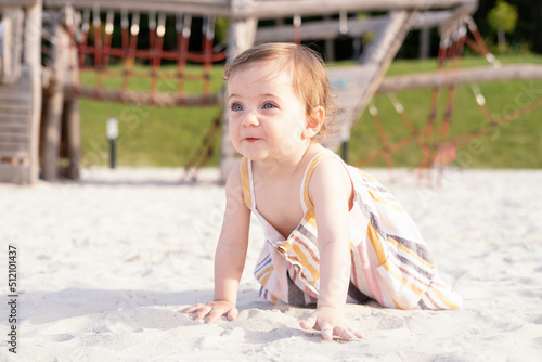 happy baby girl sitting on the beach on sand wearing striped summer dress on sunny day
