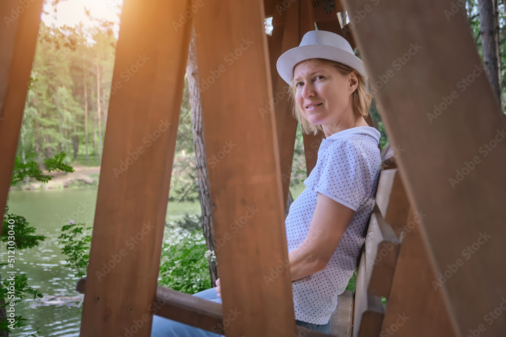 Young woman sitting on steady wooden swing in park enjoying nature on summer day.