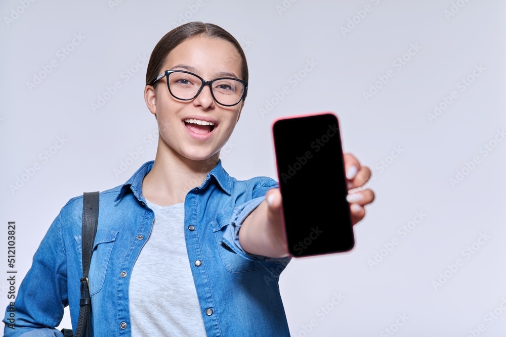Smiling teenage female student showing blank smartphone screen, light background