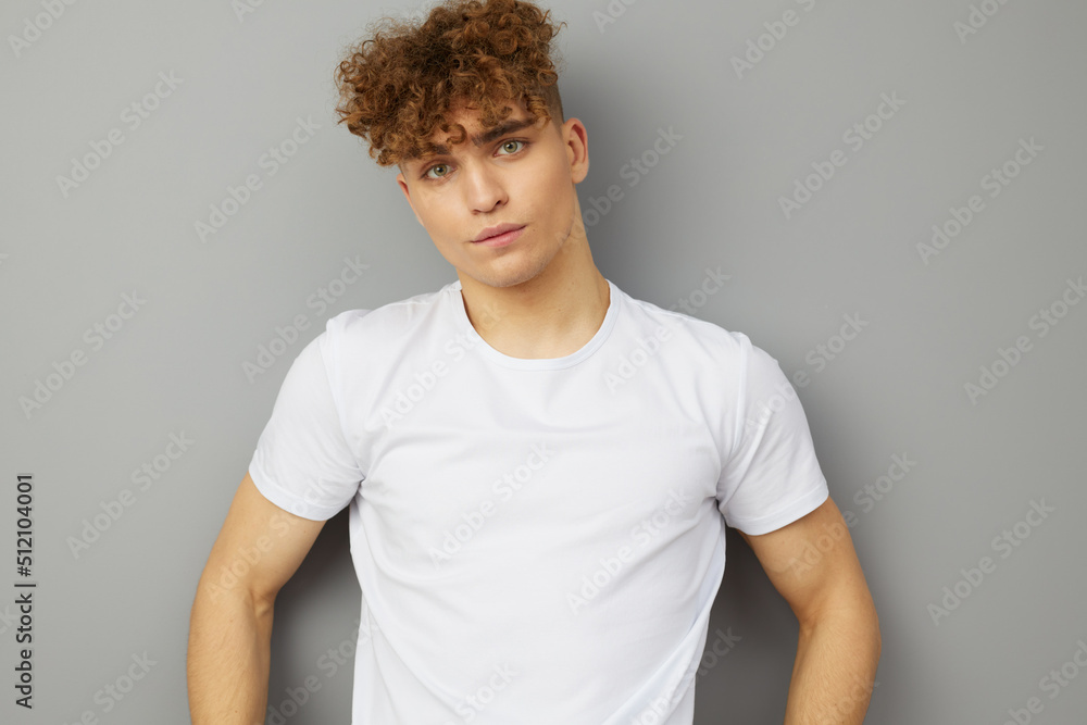 a relaxed, handsome man with curly hair stands on a gray background in a casual white T-shirt, looking pleasantly at the camera. Studio photography a relaxed, handsome man with curly hair stands on a gray background in a casual white T-shirt, looking pleasantly at the camera. Studio photography