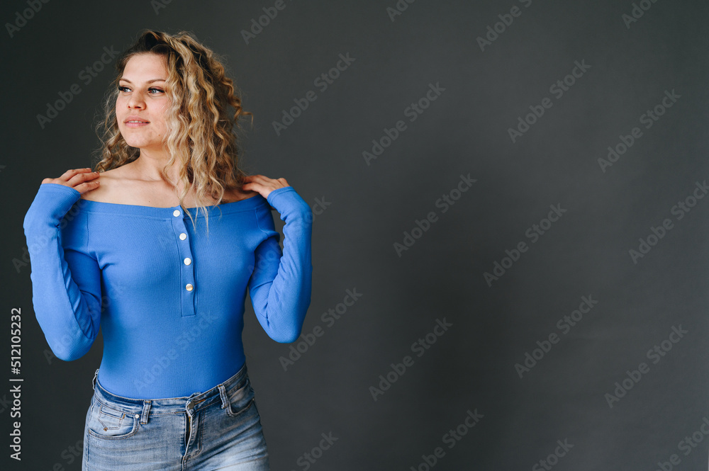 Curly Blonde On An Isolated Black Background In A Blue Sweater. Militantly Look Away. Hands rest on shoulders. Concept girl on banner Curly Blonde On An Isolated Black Background In A Blue Sweater. Militantly Look Away. Hands rest on shoulders. Concept girl on banner