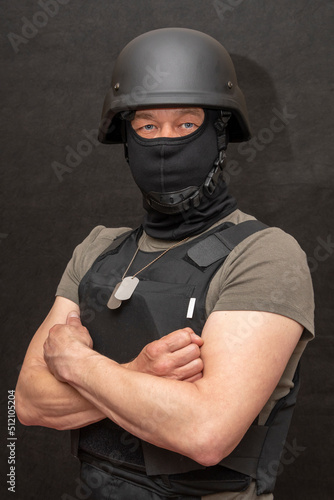 muscular military 45-50 years old in a bulletproof vest and balaclava, army helmet on his head, black background. Concept: volunteer at war, war in Ukraine, civil self-defense, army unit. © Anelo