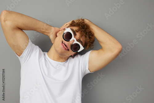 a funny young man stands in a casual T-shirt with funny glasses on his face and pleasantly smiles broadly at the camera showing yaik holding his hands behind his head photo