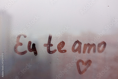 Lettering Portuguese text Eu te amo I love you in english and heart shape on sunset wet window photo