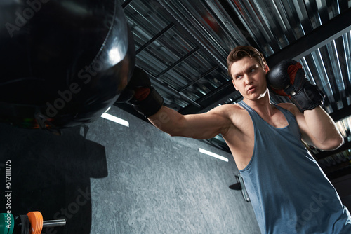 Focused muscular guy training in boxing gloves