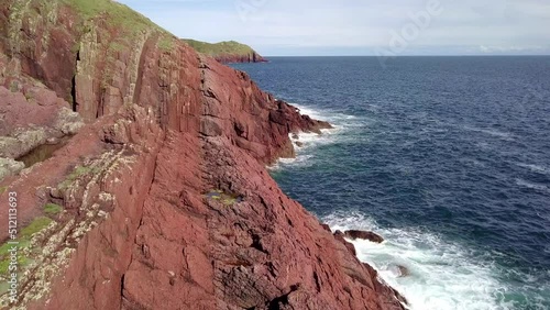 Drone ariel footage of red Welsh cliffs with blue sky's and crashing waves photo