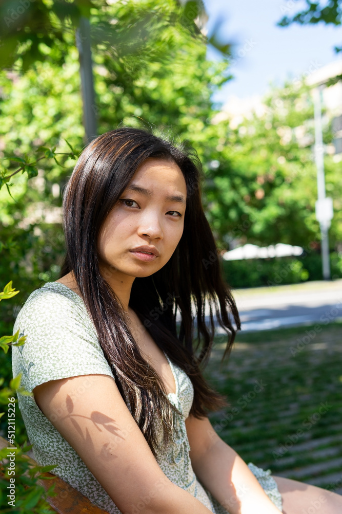 Calm Asian woman sitting on bench in park Calm Asian woman sitting on bench in park