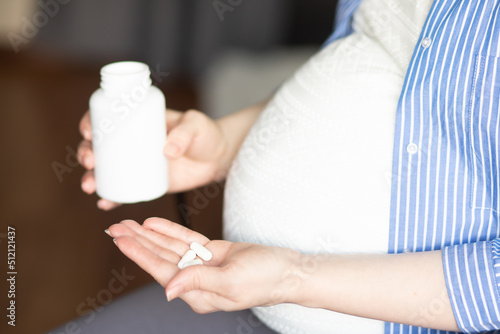 pregnant woman takes vitamins at home, pours pills into her hand