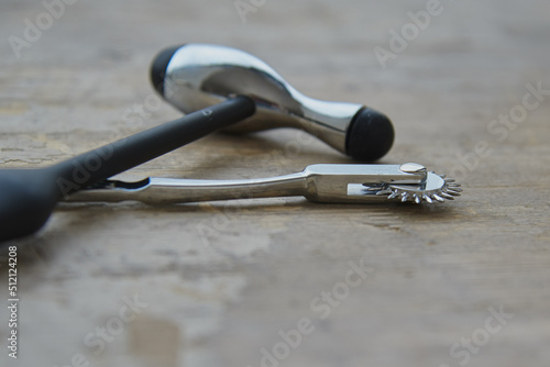 A medical hammer and a Wartenberg wheel lie on a gray wooden surface.