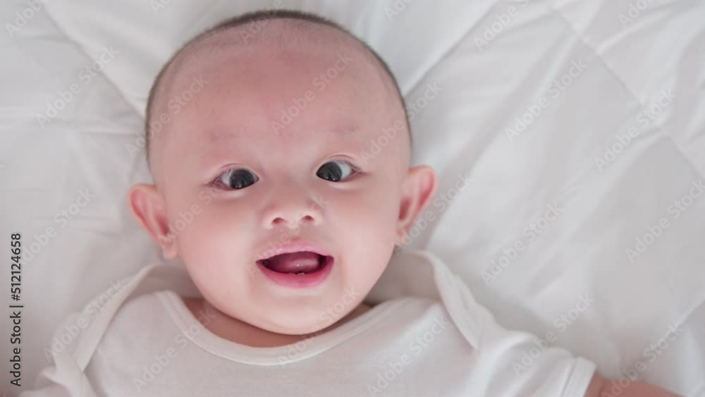 Close-up portrait of face cute asian newborn baby lying play on white bed look at camera with laughing smile happy face. Innocent little new infant adorable. Parenthood and Mother Day concept. Close-up portrait of face cute asian newborn baby lying play on white bed look at camera with laughing smile happy face. Innocent little new infant adorable. Parenthood and Mother Day concept.