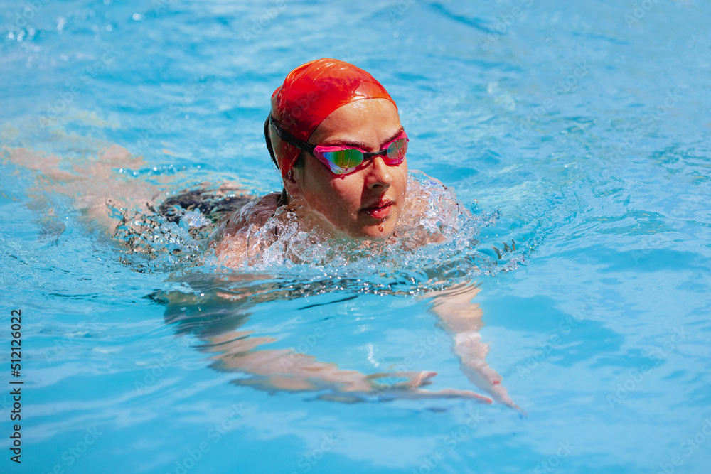 One female swimmer in swimming cap and goggles training at pool, outdoors. Healthy lifestyle, power, energy, sports movement concept.