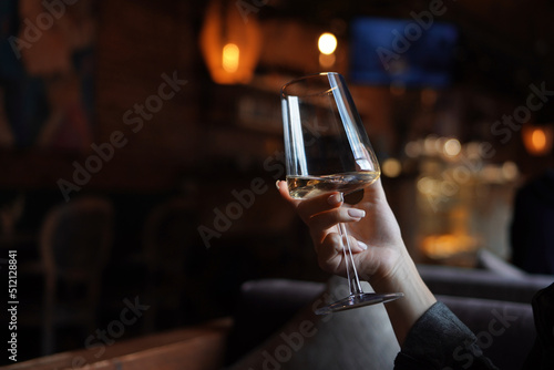 Female hand with french manicure holding a glass with wine on naturally blurred background. Woman in restaraunt. Luxury pasttime, celebration concept. 