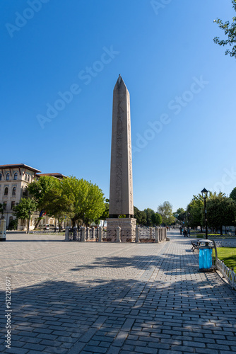 Obelisk of Theodosius seen from one end of the square, with a completely blue sky in the morning. With trees around.