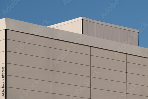 The wall of a commercial building made of precast concrete panels and metal beams. The spaces between the concrete pillars are thin spacing. The cream and textured panels are on a construction site.