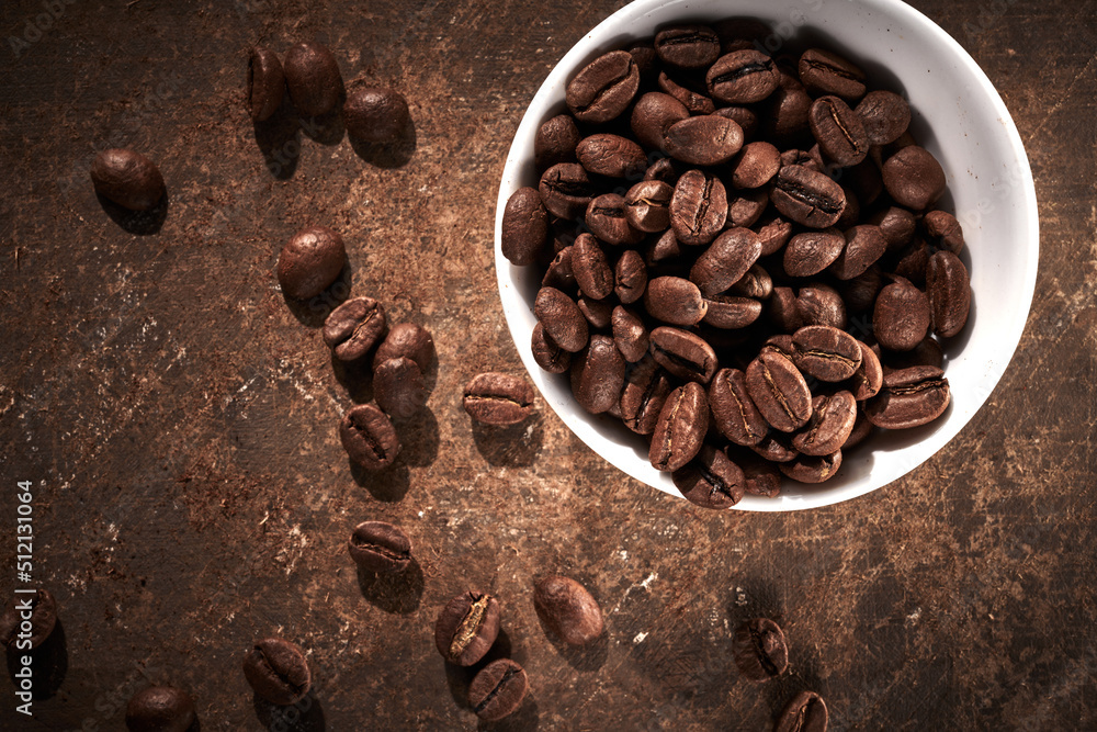 Roasted coffee beans in bowl isolated close up on brown grunge background Roasted coffee beans in bowl isolated close up on brown grunge background
