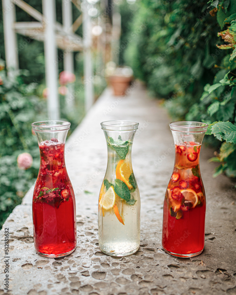 Three glass jugs of fresh berry and fruit lemonades in the garden Three glass jugs of fresh berry and fruit lemonades in the garden
