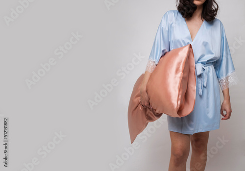 Woman in silk pajama holding silk pillow on gray background, copy space photo