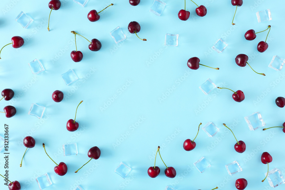 Creative layout made of cherry and ice cubes on blue background. Border arrangement. Flat lay. Minimal summer fruit concept.