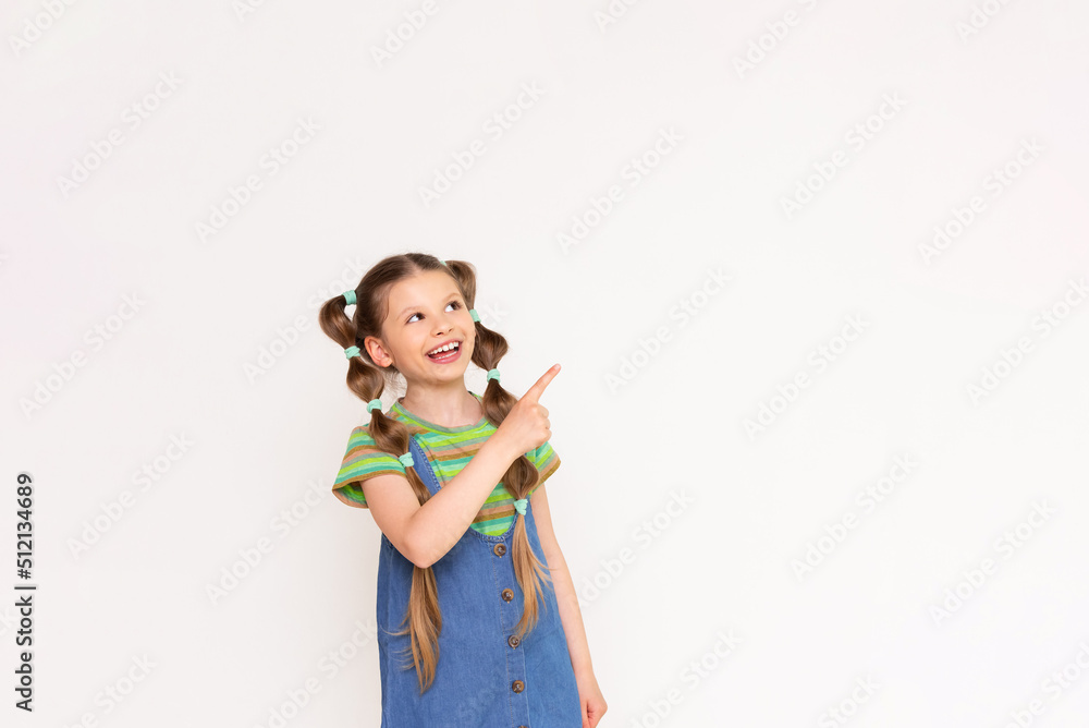 The child points his finger at your advertisement on a white isolated background. A beautiful little girl in a denim sundress. The child points his finger at your advertisement on a white isolated background. A beautiful little girl in a denim sundress.